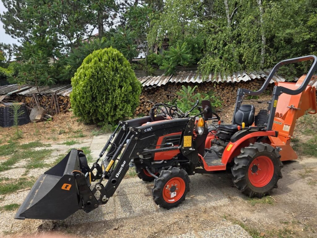 Kubota kistraktor Quicke homlokrakodóval, mögötte a narancssárga ágaprító